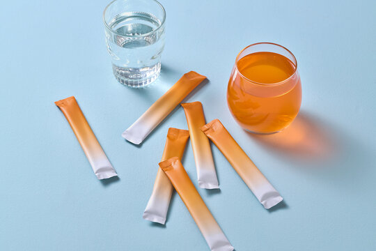 Image of a vibrant orange drink next to supplement powder sticks