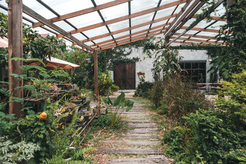 A cozy outdoor cafe surrounded by lush green garden, wooden pergola walkway, rustic architecture, natural ambiance, peaceful seating area and relaxing vibe perfect for nature lovers