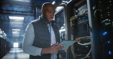 Data center technician inspects server racks, checks network cables.