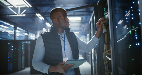 Data center technician inspects server racks, checks network cables.