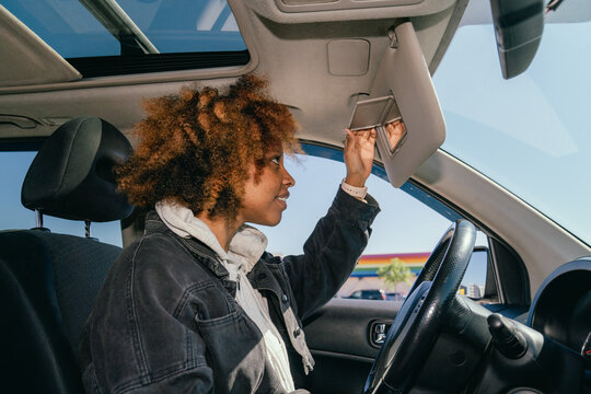 Woman looking in car sun visor mirror while 