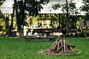 Campfire area surrounded by wooden benches and lush greenery in outdoor nature setting, perfect for group gathering, relaxation, eco-living, forest camping experience, and rustic open-air adventure