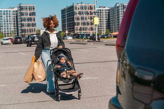 Mother carrying groceries while pushing stroller in parking lot
