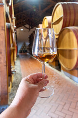 Visit of wine cellar with old large oak barrels, hand holding glass of fortified dry or sweet tasty marsala wine from barrels in Marsala, Sicily, Italy