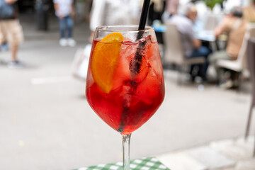 Spritz Campari red bitter long drink cocktail maid with liqueur, prosecco sparkling wine, ice cubes and piece of orange, street view of Palermo, Italy