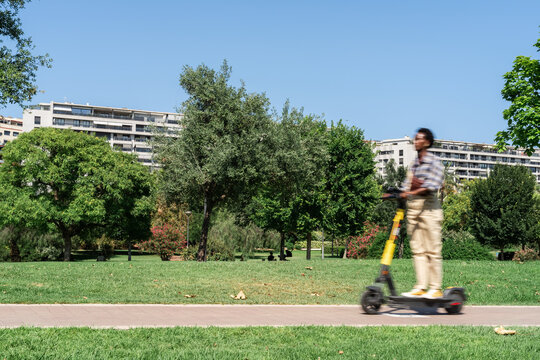 Young Woman Riding Electric Scooter Through City Park on Sunny Day - Powered by Adobe