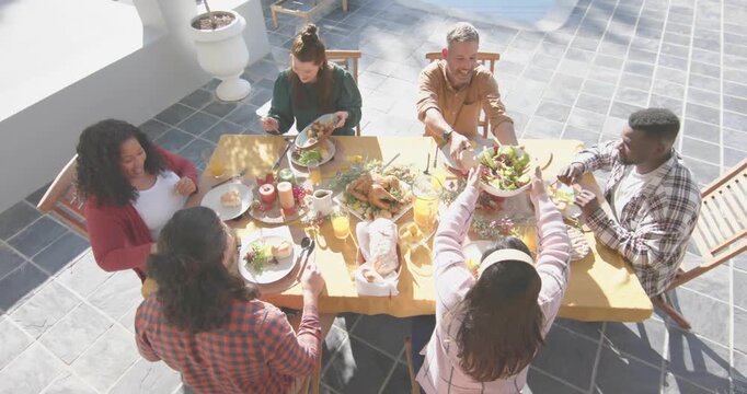 Friends picking up cutlery starting social dining on sunlit patio, sharing dishes and toasting