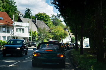 Cars waiting in traffic on a city street with houses in the background. A typical urban transportation scene.