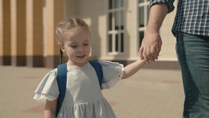 Dad leads the child by hand to school, close-up, a little schoolgirl with backpack, a happy family,...