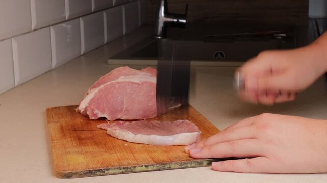 tenderizing raw pork cutlet with meat mallet on wooden cutting board in kitchen. preparing pork chops for cooking. concept of meat preparation, home cooking, culinary process