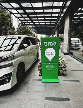 31.05.2025, Kuala Lumpur, Malaysia. Green Grab sign for pick up and drop off beside a parked white car on a city street. Modern urban background with glass and buildings.