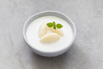 Children Milk soup with cottage cheese quenelles. Decorated with fresh mint. Light background
