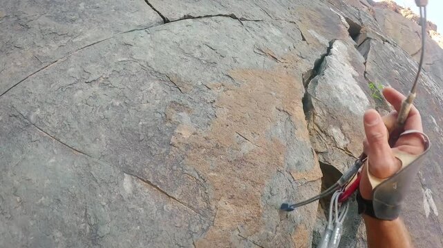 Climber's hand placing gear on rocky cliff face