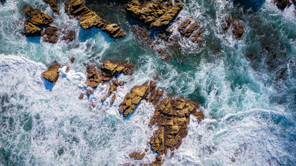 Aerial shot of rocky seashore with waves splashing over stones and blue green sea powerful natural...