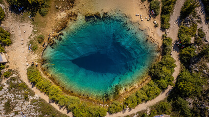Aerial photo of Cetina River spring in Croatia with deep blue natural pool surrounded by rocky landscape and greenery unique travel nature spot