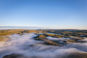 Aerial view of Nordkapp Norway with mountain landscape partly covered in low clouds under clear blue sky remote Arctic scenery and travel destination