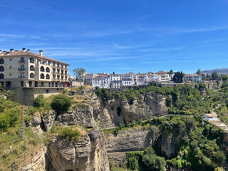 Fototapeta premium Stunning panoramic view of Ronda, Spain: Picturesque white buildings on cliffs above the El Tajo gorge under a clear blue sky