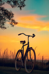 Obraz premium Sunset Bicycle Silhouette: A vintage bicycle stands silhouetted against a stunning sunset backdrop, with its curved handlebars and detailed frame showcased in a picturesque outdoor scene. 