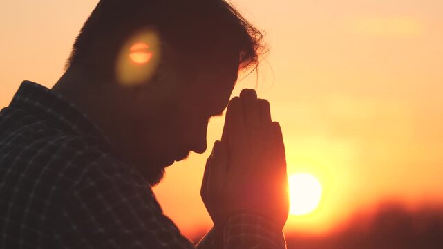 An adult man prays at sunset in the sky, religious faith, ask for forgiveness and regret the past done, dream to be and live better, a man in the glare of the sun at dawn.