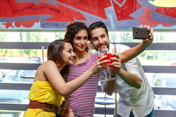 Naklejka premium Friends taking selfie while drinking cocktails in a pub