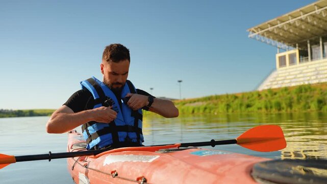 Kayaker fastening life vest and holding paddle in kayak