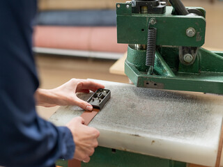 A woman makes holes in a leather belt in a workshop.