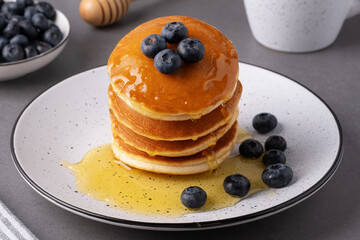Fluffy pancakes topped with blueberries and syrup served on a white plate at a breakfast table
