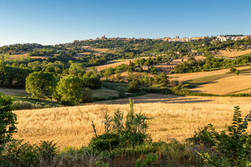 Countryside landscape with a harvested golden field in the foreground and a view of the city of...