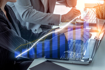 Two business professionals interpret financial data on laptops, showcasing graphs and charts that represent market trends in a modern workspace. Impute