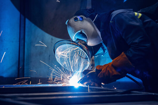 Factory industrial welder worker in workplace with spark, neon light. Professional welder fix industry truck