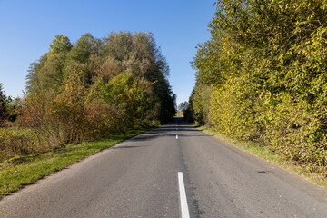 a wide road in rural areas, autumn nature with deciduous trees during the color change of foliage and an asphalt road in eastern Europe