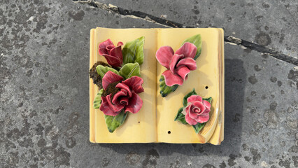 Ceramic memorial book with sculpted roses on a stone tomb