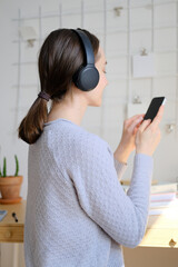 Happy girl listening to music online with wireless headphones from smartphone. Woman is having fun with music with a phone and headphones. Girl uses wireless earphones