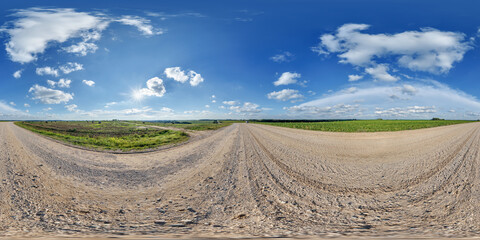 hdri 360 panorama view on gravel country roads among fields with clouds in sky in equirectangular...