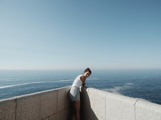 A girl on a stone balcony high up on the cliff with the sea and sky in the background. 