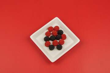 Plate with red and black berry-shaped gummi candy in the foreground on a red background