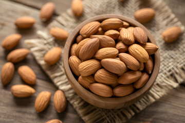 Bowl of Almonds: A close-up shot of a rustic wooden bowl overflowing with wholesome, raw almonds, artfully arranged on a textured surface, inviting a celebration of nature's healthy bounty.