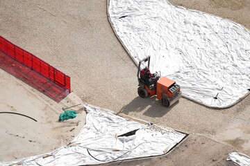 Worker operating small road roller on gravel surface during road construction site preparation
