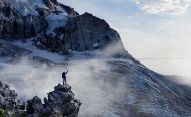 Man Standing on a Rocky Cliff Near Icy Mountains in Morning Mist