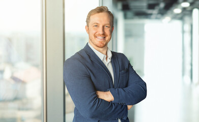 Handsome man business professional stands in an office setting, smiling confidently and looking at the camera. He wearing professional attire, man in the front has his arms crossed