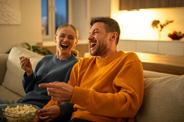 Smiling young couple enjoying popcorn watching movie together on living room sofa. Couple...