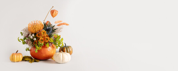 Creative autumn floral arrangement of seasonal flowers in pumpkin as vase on gray background for Thanksgiving Day. Annual decorations. Copy space. Banner.