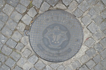 Manhole cover featuring Lisbon's emblem on cobblestone street in Lisboa, Portugal showcasing local craftsmanship and design