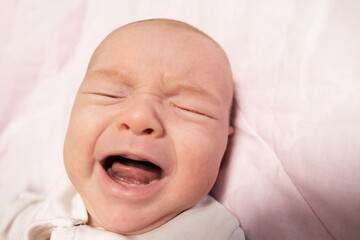 Little two month old newborn baby boy is crying. Screaming hungry infant face portrait close up. Baby experiences pain during colic in the abdomen