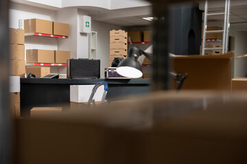 Empty desk in a shipping area framed by taped boxes and shelves, representing local brand small business operations and logistics. Industrial small scale workstation in supply room.