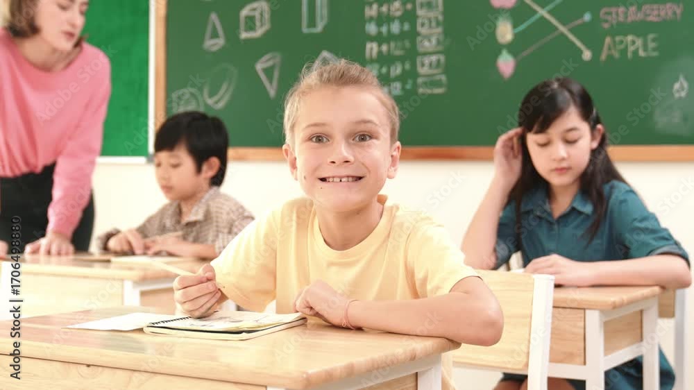 Poster caucasian smart child smiling at camera while doing classwork at classroom while happy multicultural