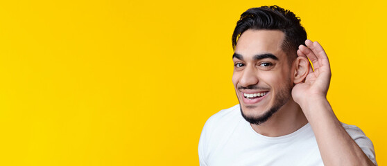 Closeup portrait of cheerful bearded arab guy eavesdropping and smiling over yellow studio...