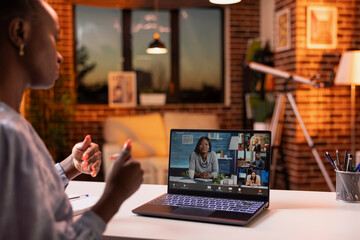 Young woman using laptop to join remote business conference call with multicultural colleagues. Female freelancer in virtual team meeting from home office, gesturing and sharing marketing ideas.