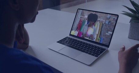 Watching woman in blue shirt viewing swatch on laptop in studio, with clothing rack, copy space