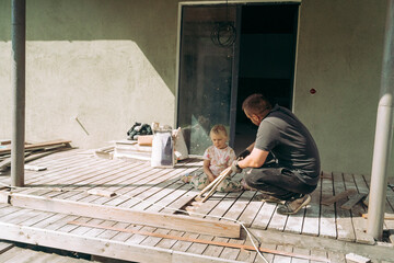 Father teaching daughter woodworking on a sunny porch